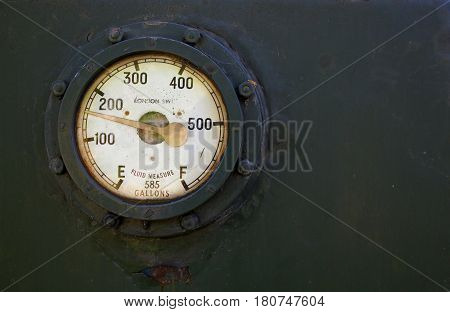 Fluid measure gauge for a train secured in place on a metal plate using nuts and bolts. Gauge measuring up to 585 gallons. With space for text.