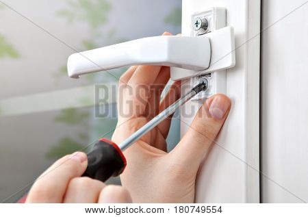 A close-up of a screwdriver in his hand unscrewing the bolt from the handle of the window frame.