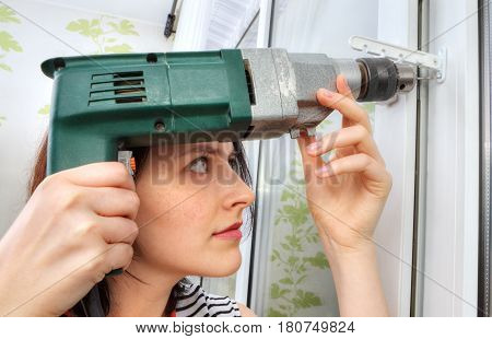 The girl makes fixing holes under the window limiter using an electric drill.