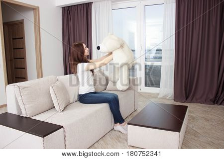young woman on the couch in the hands white teddy bears in new fashioned style room.