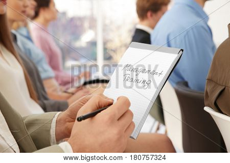 Man holding notebook with text MANAGEMENT TRAINING at business presentation