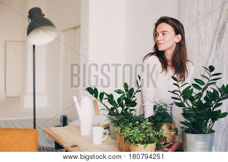 young woman watering flowerpots at home. Casual lifestyle series in modern scandinavian interior