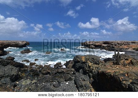 A scenic look on Aruba's black sand beach with rugged lava rocks.