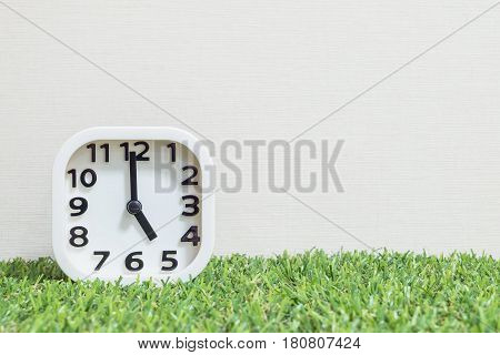 Closeup white clock for decorate in 5 o'clock on green artificial grass floor and cream wallpaper textured background with copy space