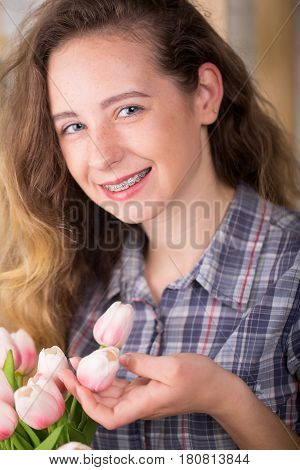 A girl with braces posing against a brick wall background with a bouquet of tulips. Dental concept