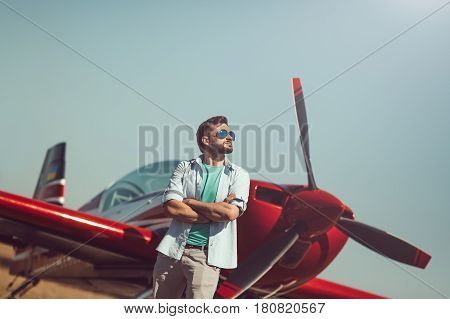 Pilot and airplane. Cheerful handsome young man pilot standing near small sport plane