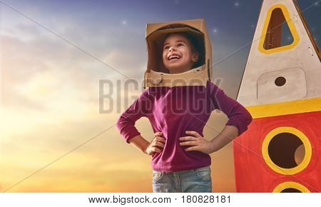 Child girl in astronaut costume with toy rocket playing and dreaming of becoming a spacemen. Portrait of funny kid on a background of sunset star sky on nature. Family games outdoors.