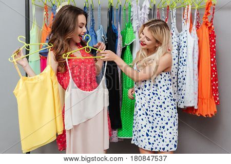 Two young beautiful women choosing the best dress near hanger with clothes