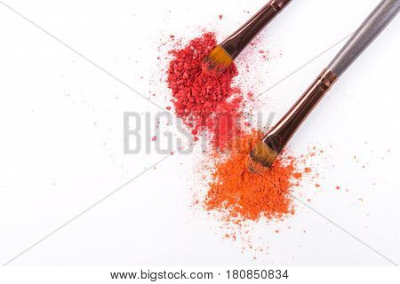 Makeup brushes with blush or eyeshadow of pink, red and coral tones sprinkled on white. Make up and female cosmetics background