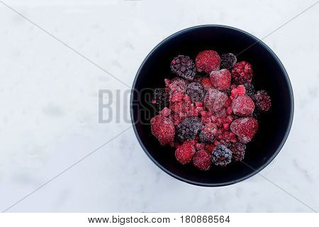 Frozen Berries in black bowl on white marble surface