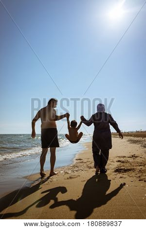 Muslim family, dad and mom with burkini on the beach walking near sea