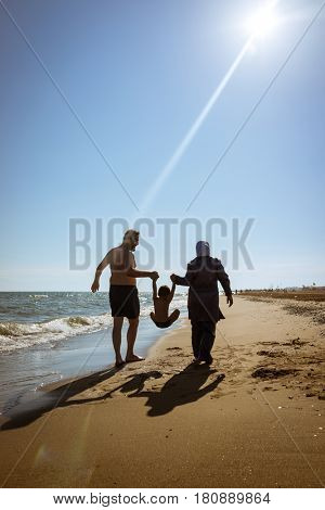 Muslim family, dad and mom with burkini on the beach walking near sea