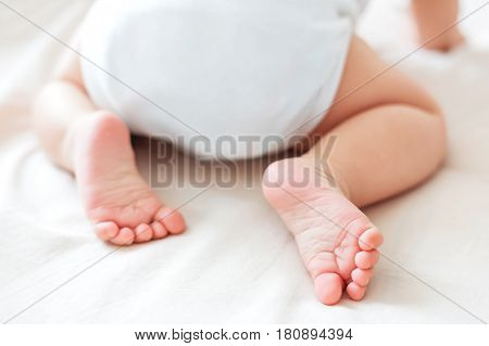 Baby's feet. Little child wearing white bodysuit and diaper. Cozy morning bedtime at home.
