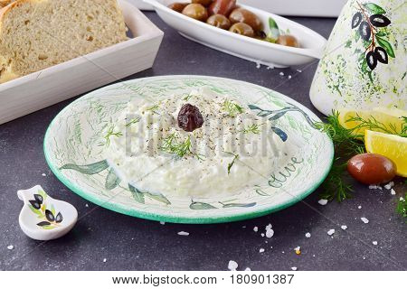 Greek traditional sauce tzatziki with olives, olive oil jar, lemon and bread on a grey abstract background. Healthy eating concept