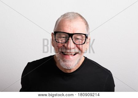Handsome senior man in black t-shirt and eyeglasses. Studio shot against white wall.
