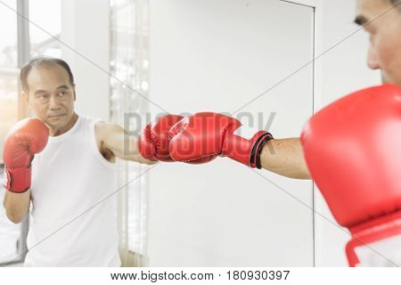 Portrait of Asian senior fighter man punching with red boxing gloves. Boxing practicing.