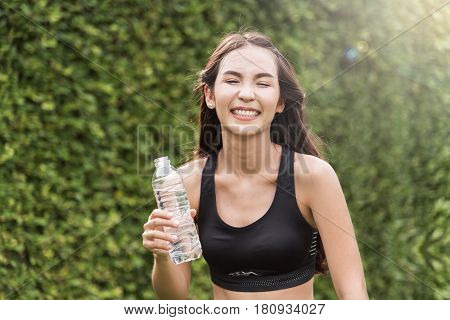 Asian woman holding bottle of water on natural background. freshness happiness relaxing and smiling.
