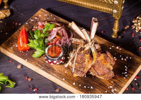 Pieces of mutton tenderloin on a stone, is served with onions, red pepper, parsley and spices salad, French fries and the Ajika sauce