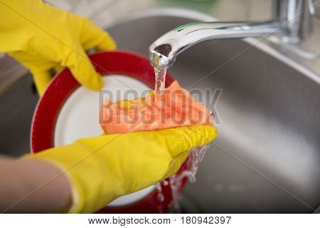 Cleaning dishware kitchen sink sponge washing dish. Close up of female hands in yellow protective rubber gloves washing