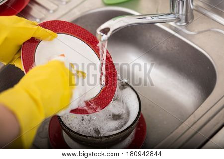 Cleaning dishware kitchen sink sponge washing dish. Close up of female hands in yellow protective rubber gloves washing