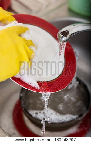 Cleaning dishware kitchen sink sponge washing dish. Close up of female hands in yellow protective rubber gloves washing