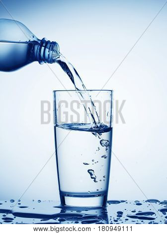 Water flowing from bottle into a glass toned in blue