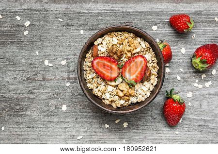 healthy breakfast strawberry muesli with oats granola and nuts in a bowl on rustic wooden table. top view with copy space