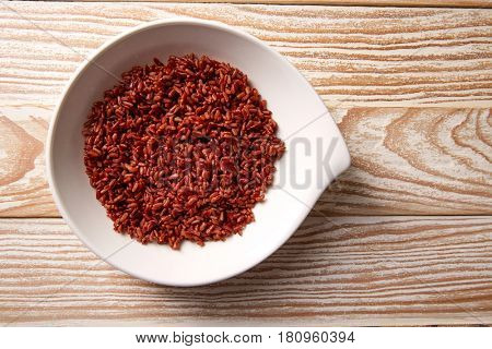 Red wild rice in a white plate over wooden board