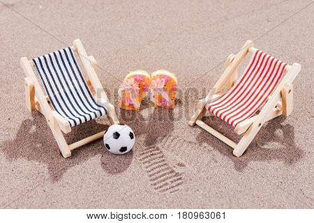 Two empty sun loungers with ball and shoes on the beach