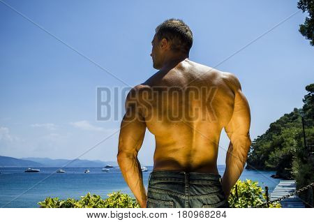 Back of young muscle man at the seaside, outdoors, showing muscular back and shoulders in front of the sea