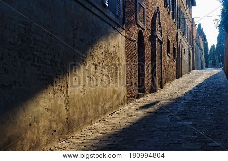 Ray of sunshine lights the brick walls and cobblestone in Vicolo di San Clemente - Siena, Italy