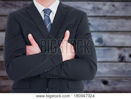 Digital composite of Business man mid section with arms crossed against blurry blue wood panel