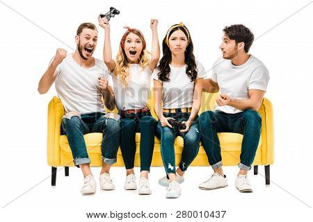 Emotional Young Friends Sitting On Couch And Playing With Joysticks Isolated On White