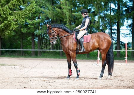 Training Process. Young Teenage Girl Riding Bay Horse On Arena At Equestrian School. Colored Outdoor
