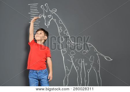 Cute Little Child Measuring Height Near Chalk Giraffe Drawing On Grey Background