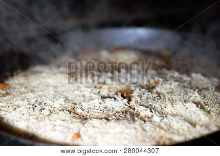 Cooking Rice For Pilaw Or Paella In Iron Cauldron Over Open Fire. Smoke And Steam. Tasty Food Prepar