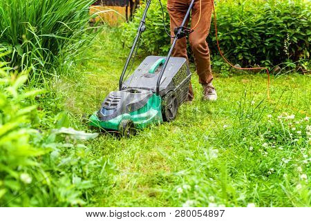 Man Cutting Green Grass With Lawn Mower In Backyard. Gardening Country Lifestyle Background. Beautif