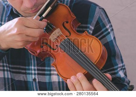 Man Adjusts The Violin Twisting The Bolts And Playing It With A Bow.