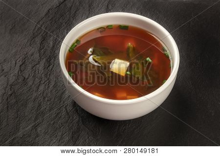 A Photo Of A Bowl Of Miso Soup With Tofu, Scallions, And Wakame Algae, On A Black Background With A 