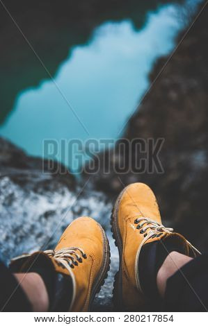 Feet Of Nature Explorer In Boots Sitting Over River Canyon