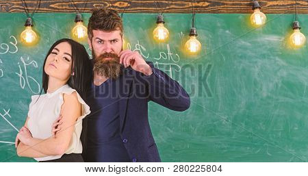 Man With Beard And Sexy Girl Teacher Stand In Classroom, Chalkboard On Background. Partners Concept.