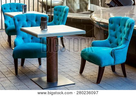 An Outdoor Cafe With Square Wooden Tables And An Iron Leg And Upholstered Armchairs With High Backs 