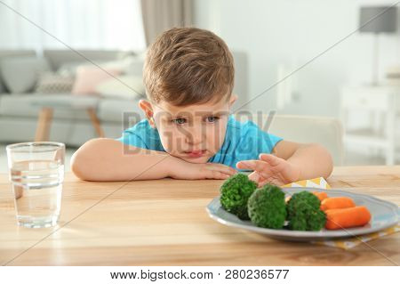 Unhappy Little Boy Refusing To Eat Vegetables At Table In Room