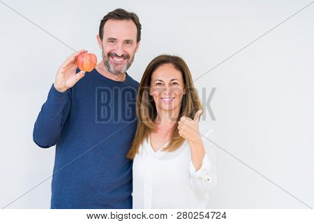 Middle age couple eating fresh apple over isolated background happy with big smile doing ok sign, thumb up with fingers, excellent sign