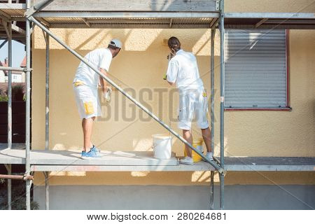 Back view of man and woman painter working coloring wall yellow