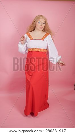 beautiful chubby caucasian blonde girl in red and white national Russian sundress on solid pink back