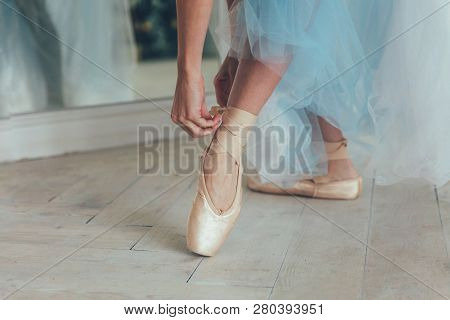 Hands Of Ballerina In Blue Tutu Skirt Puts On Pointe Shoes On Leg In White Light Hall. Young Classic