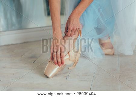 Hands Of Ballerina In Blue Tutu Skirt Puts On Pointe Shoes On Leg In White Light Hall. Young Classic