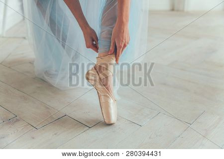 Hands Of Ballerina In Blue Tutu Skirt Puts On Pointe Shoes On Leg In White Light Hall. Young Classic