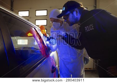 Crime Investigation - Police Technician Showing Fingerprints To Colleague On Suspected Car In Garage
